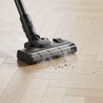 Aspirateur balai sans fil noir sur parquet clair en plein nettoyage