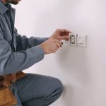 Electricien agenouille installe interrupteur double sur mur blanc d une piece