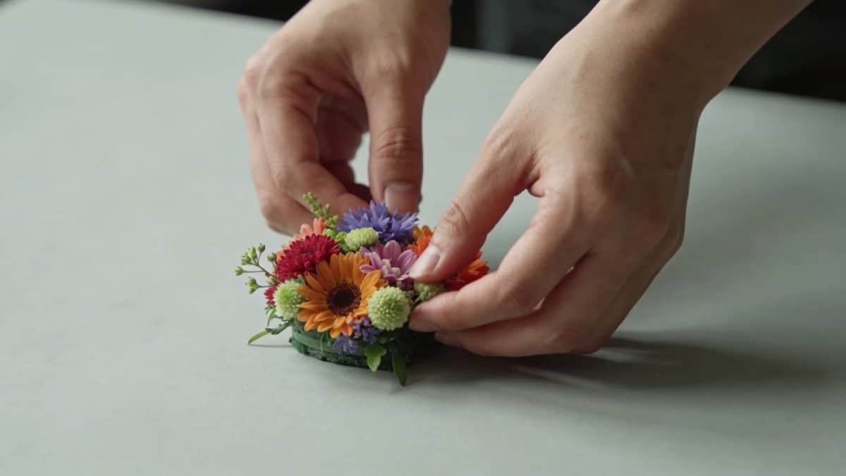 Gros plan mains arrangeant une petite composition florale colorée sur table
