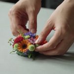 Gros plan mains arrangeant une petite composition florale colorée sur table