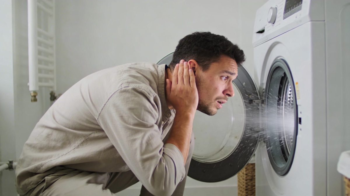 Homme inquiet penche oreille vers machine a laver vrombissante en marche