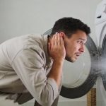 Homme inquiet penche oreille vers machine a laver vrombissante en marche