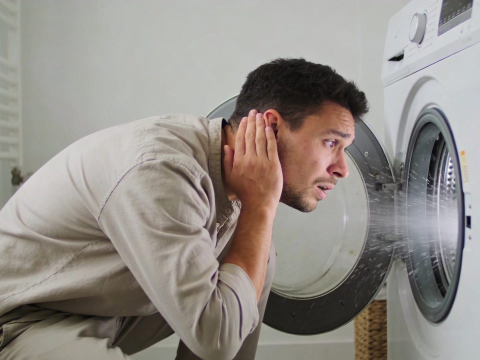 Homme inquiet penche oreille vers machine a laver vrombissante en marche