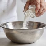 Main de cuisinier versant poudre blanche d oseille dans bol en inox