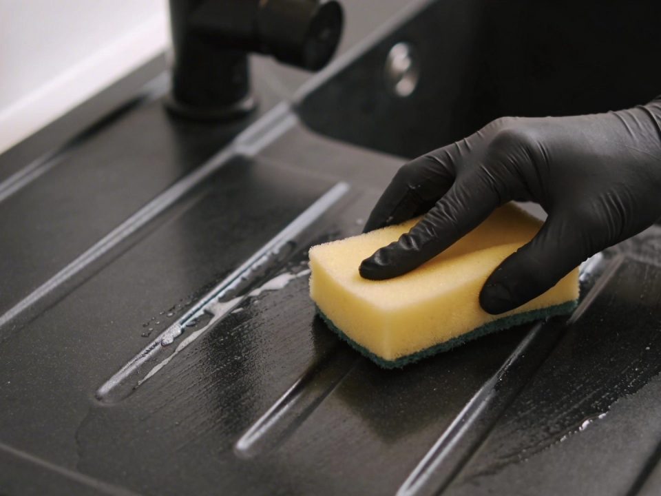 Main noire frottant evier noir en resine avec eponge jaune