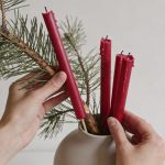 Mains disposant des branches de sapin et bougies rouges dans un vase