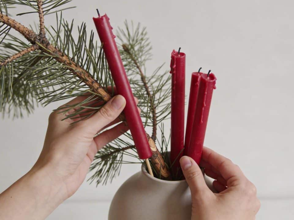 Mains disposant des branches de sapin et bougies rouges dans un vase
