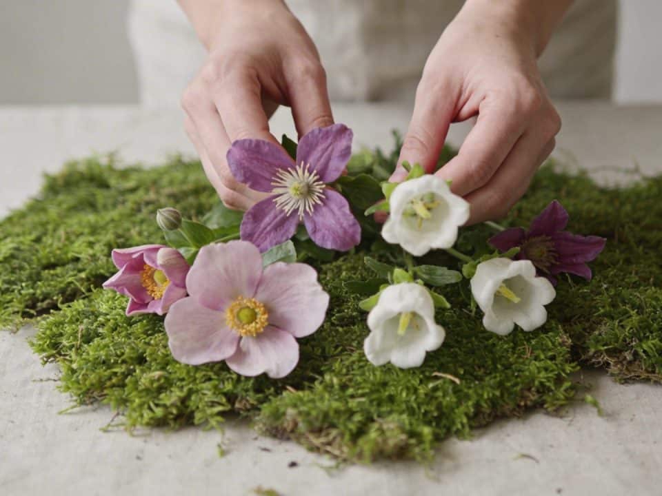 Mains disposant des fleurs fraiches dans la mousse verte sur table