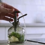 Mains versant liquide vegetal dans vaporisateur en verre sur table de cuisine