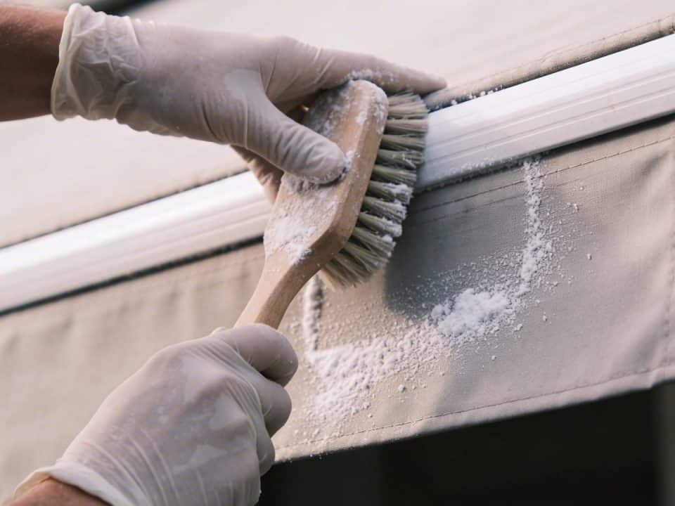 Personne frottant un store banne exterieur avec une brosse et bicarbonate
