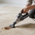 Personne nettoyant une tache tenace sur tapis beige avec petit aspirateur portatif
