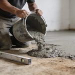 Ouvrier agenouille verse beton gris sur sol prepare avec regle metal