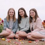 Trois petites filles souriantes assises dans un champs de tulipes colorées