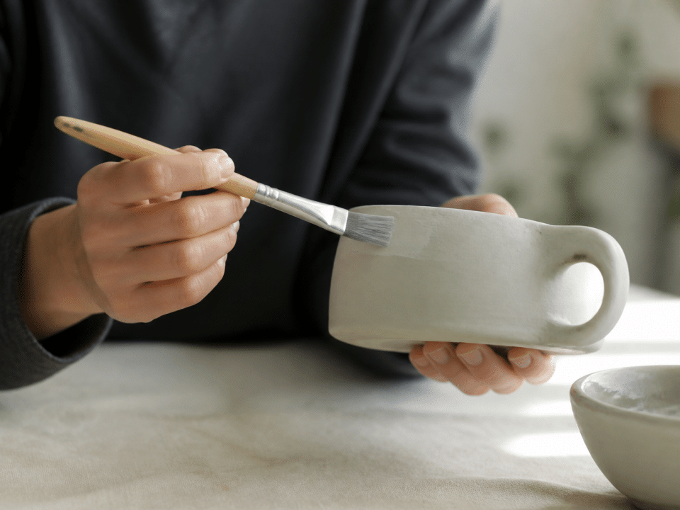 Mains tenant tasse blanche posee horizontalement avec pinceau